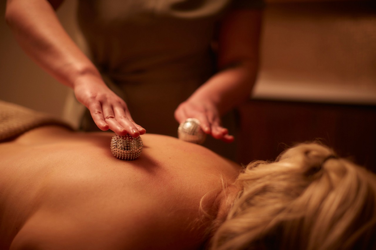 Woman having metal balls rolled against her back.
